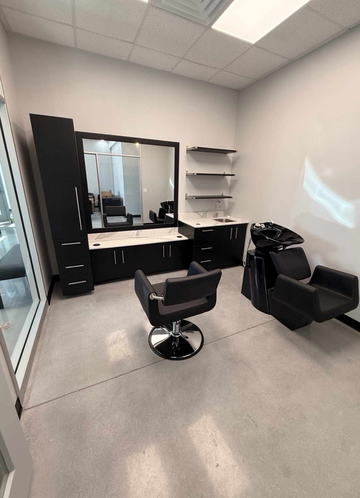 A private salon suite with styling chair, mirror, quartz counters and a shampoo bowl